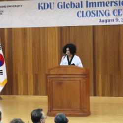 Visão de um palco com o estudante Iago ao centro, falando ao microfone